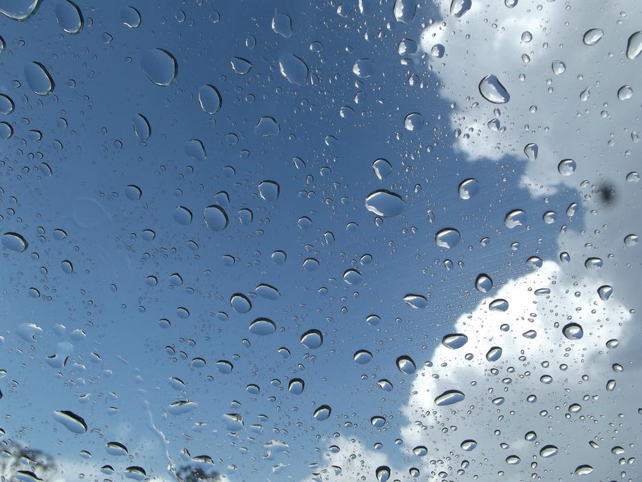Beautiful water drops on the window, at blue sky with white clouds on background