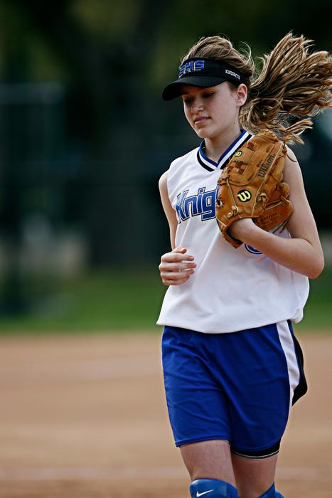 Beautiful, blonde softball girl payer in white and blue uniform, with the globe, on the field