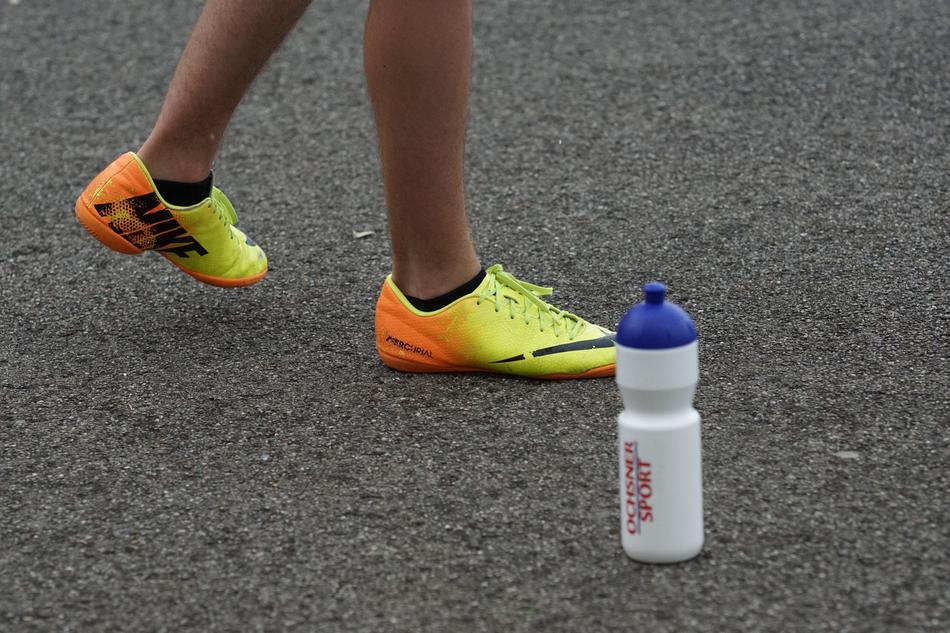 Close-up of the legs of a person, with the colorful 'Nike' soccer shoes, near the bottle