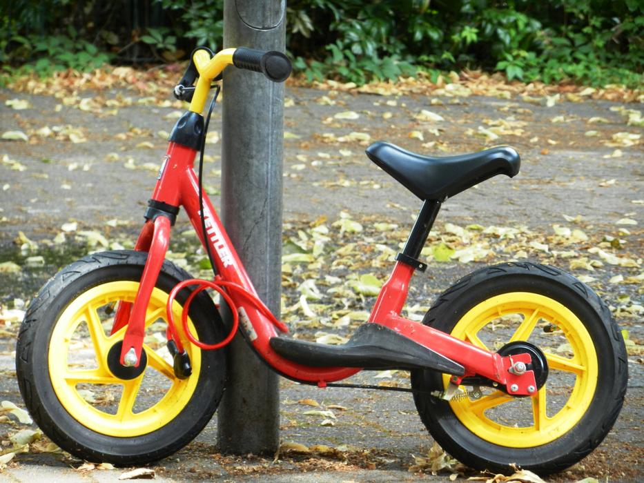 red kids balance bike near the post in autumn