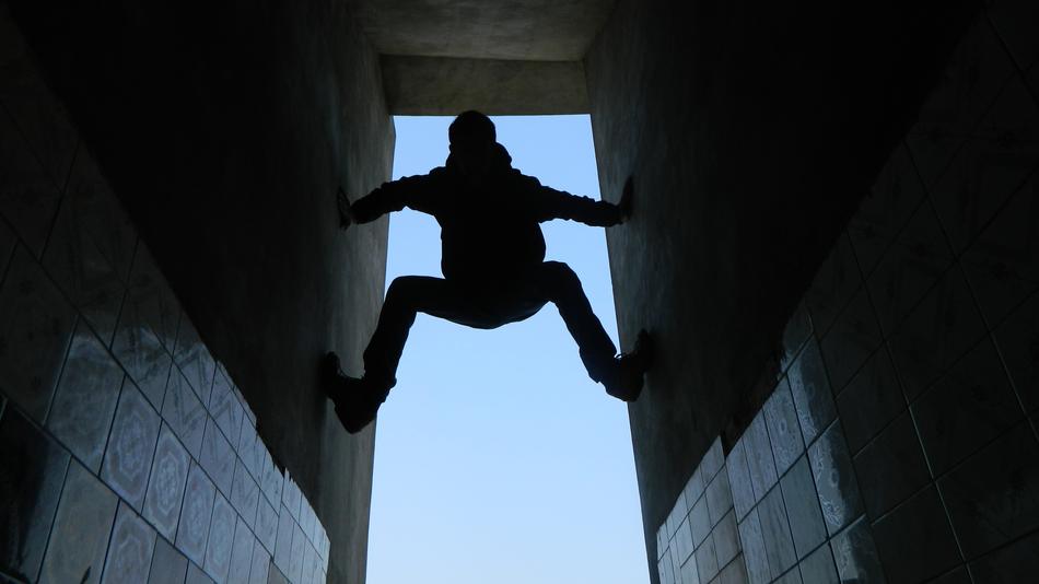 Silhouette of a boy, climbing on the walls, at blue sky on background