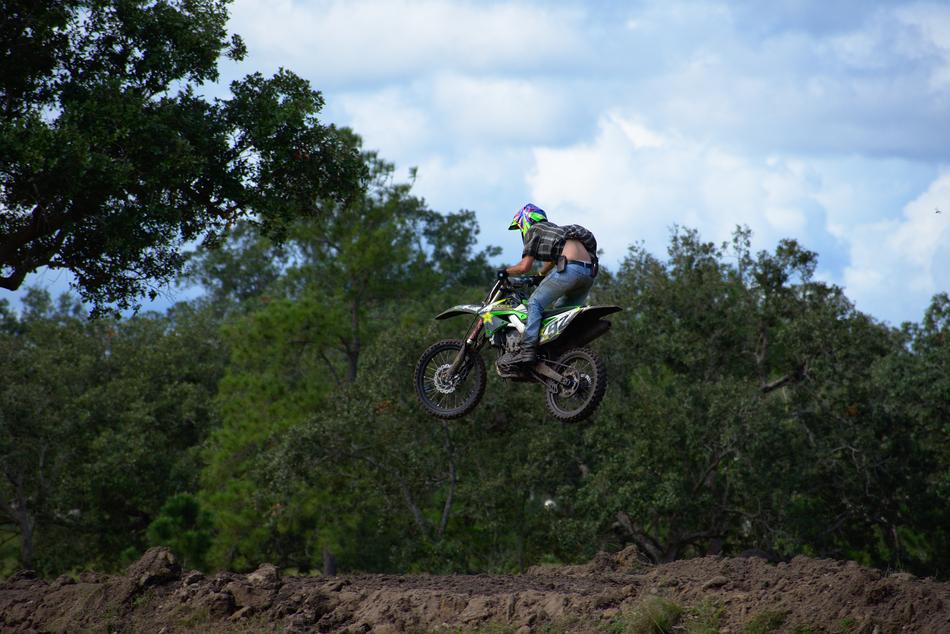 Bike rider in jump, near the green plants, under the blue sky with clouds