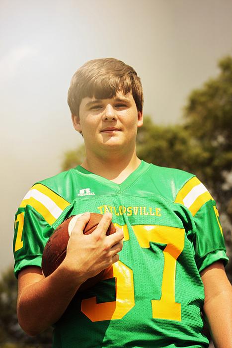 American football player boy in colorful uniform, with the ball, in light