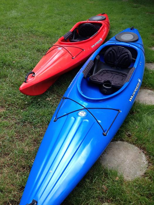 Shiny, blue and red kayaks on the green grass and stones