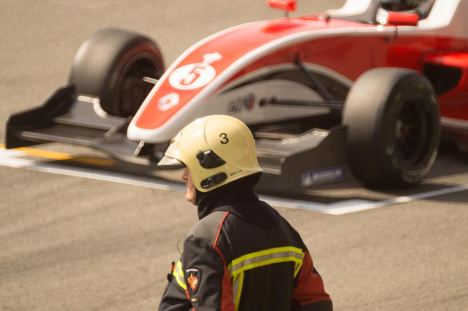 Fireman near the red and white race car on the road in sunlight, on the Formula One