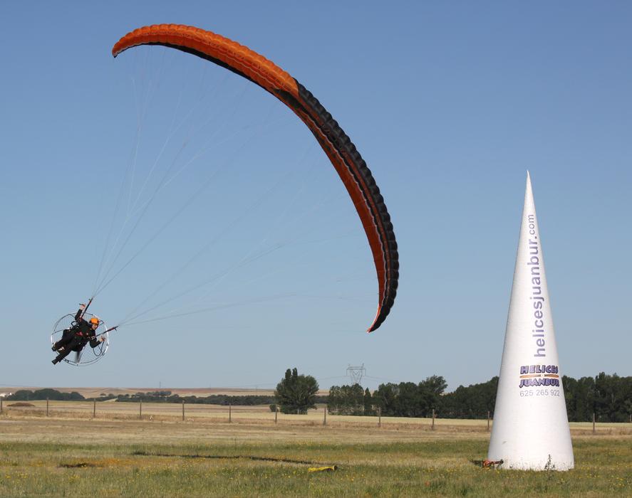 Person flying on the paramotor, above the colorful and beautiful plants, under the blue sky