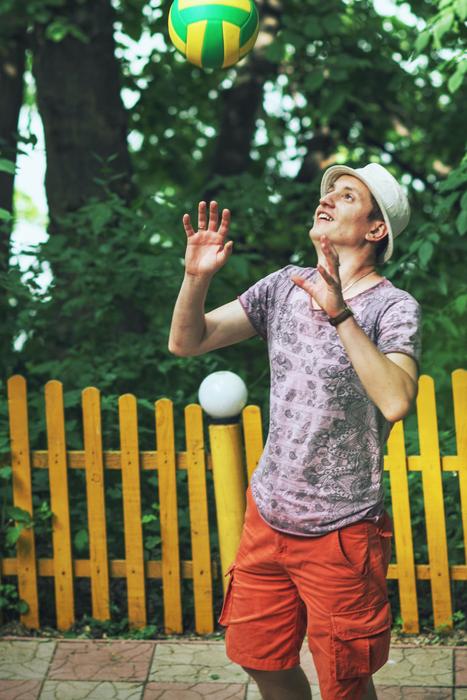 Guy playing volleyball near the yellow and orange fence and green plants