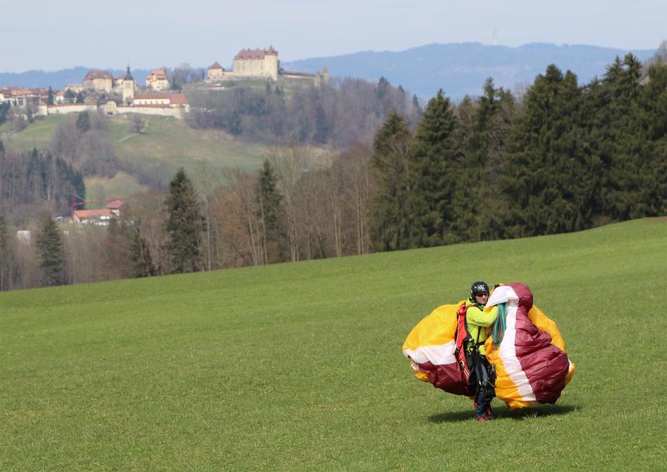 Paraglider with colorful parachute, on the beautiful, green meadow among the trees, near the buildings, in Switzerland
