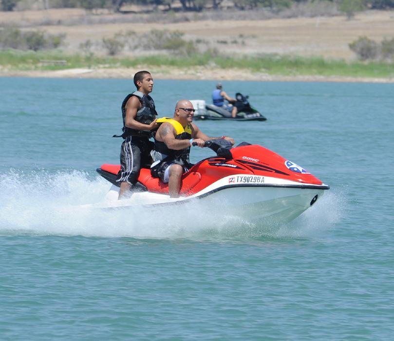 People, riding on the jetski, on the beautiful, turquoise water with ripple, near the colorful shore