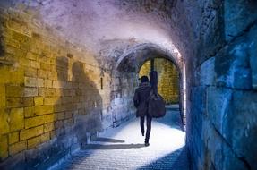 a man with a guitar walking down the tunnel