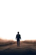 silhouette of man walking on road through meadow