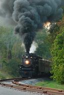 Steam Locomotive with black smoke from chimney speeding on Railway at evening