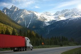 Truck on Road near warning traffic sign at scenic snow capped mountains, canada