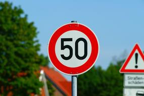 Red, black and white road signs, near the green trees and buildings, at blue sky on background