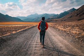 young man with a backpack walks along a mountain road