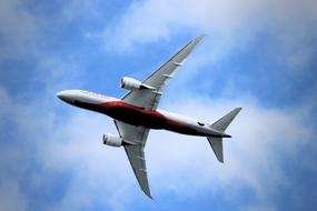 Bottom view of the red and white jet, flying in the beautiful blue sky with white clouds