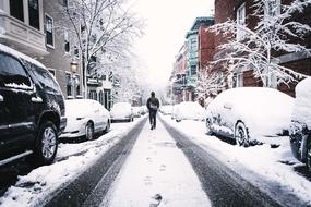 Man, walking on the beautiful, frozen street with the snow and cars, among the colorful buildings in winter