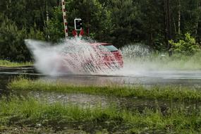 red car in a puddle on the road in front of the barrier