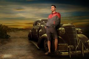 a man stands near an old car at sunset