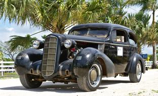 Beautiful, antique, black, classic car on the road near the white fence and green and yellow palm trees