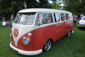 Beautiful, shiny, white and red Volkswagen Kombi car, among the people, near the other car, on the green meadow, among the trees