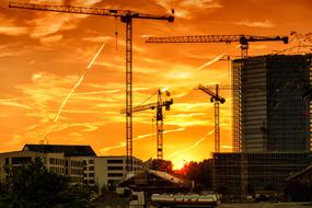 Cranes on the site, among the buildings, at colorful and beautiful sky with the clouds