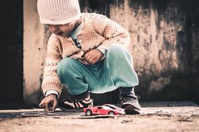 Baby in the cap and clothing, playing with the colorful, shiny toy cars, in light