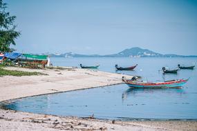 Colorful boats on the water near the shore, with the green trees, and beautiful mountain on background, in Thailand