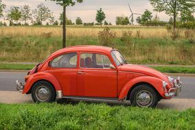 Beautiful, retro, red VW Beetle car, on the road, among the green and yellow fields