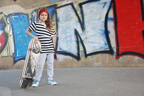 Girl, with the skateboard, near the colorful and beautiful graffiti on the wall