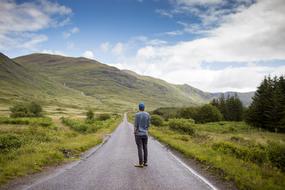 the guy stands on the road in the countryside against the background of mountains