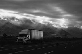 truck on a highway against a background of mountains and a cloudy sky, black and white