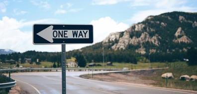 "One Way" road sign on the beautiful winding road, among the green mountains