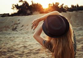 girl in a hat on the beach closes her hands from the sun