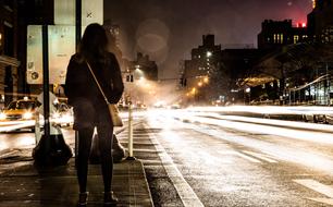 Person with back, standing near the road in the city with colorful lights, at night