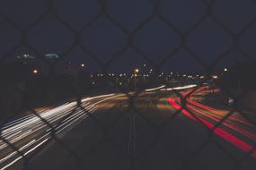 traffic on Bridge at night, view through wire mesh fence