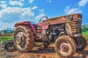 Colorful, old, rusty tractor on the colorful field, under the blue sky with white clouds