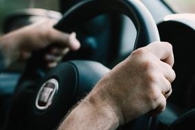 male hands on car steering wheel close up on blurred background