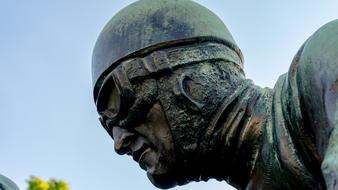 Head of the sculpture of race car driver, with the glasses, and in helm, near the yellow sunflowers, at blue sky