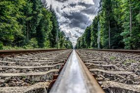 Railroad Track through forest under cloudy sky