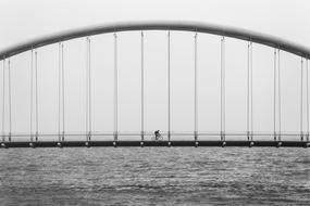 black and white photo of a biker on a suspension bridge