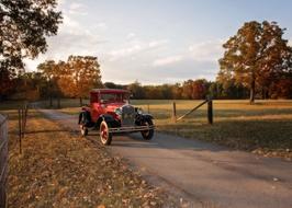 Beautiful, retro, red Ford car on the road, among the colorful plants in autumn