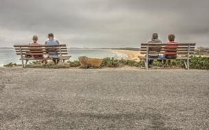 two couples are sitting on wooden benches on the sea coast