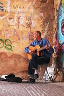 man plays guitar on street at grunge wall