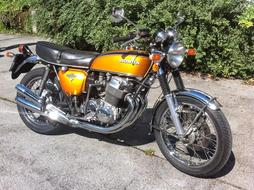 Orange and black, shiny Honda Cb 750 motorcycle on the asphalt, near the green plants