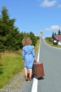 woman with brown suitcase at the edge of the road on a sunny day