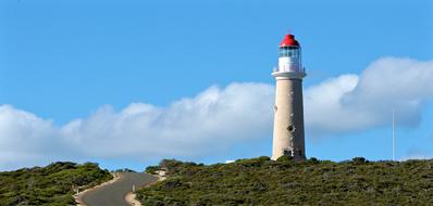 Beautiful landscape with the lighthouse, among the green plants on the mountain, at blue sky with clouds on background