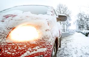 Beautiful, red car with bright headlight, in snow, among the trees, in winter