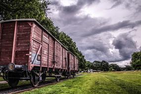 Freight cars of a train on rails among the green fields and trees on beautiful landscape under cloudy sky