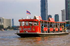 Colorful boat, with the flag of Thailand, on the Chao Phraya River, near the buildings
